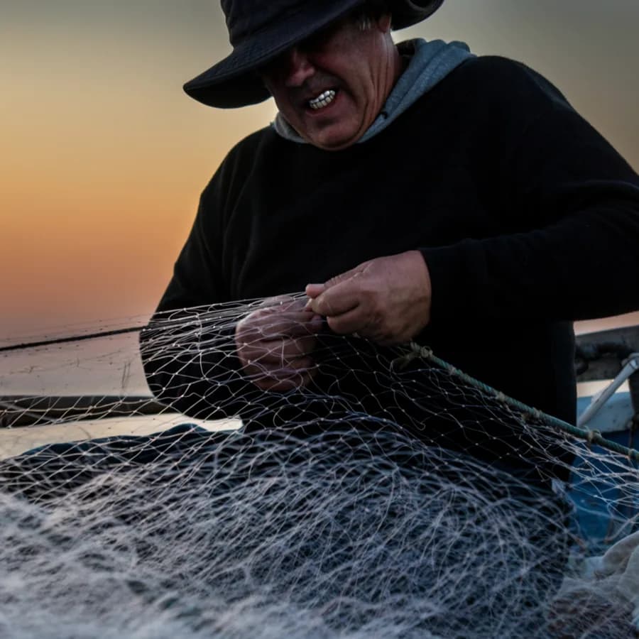 Documentary-style photo of a fisherman mending nets at dawn, weathered hands in focus